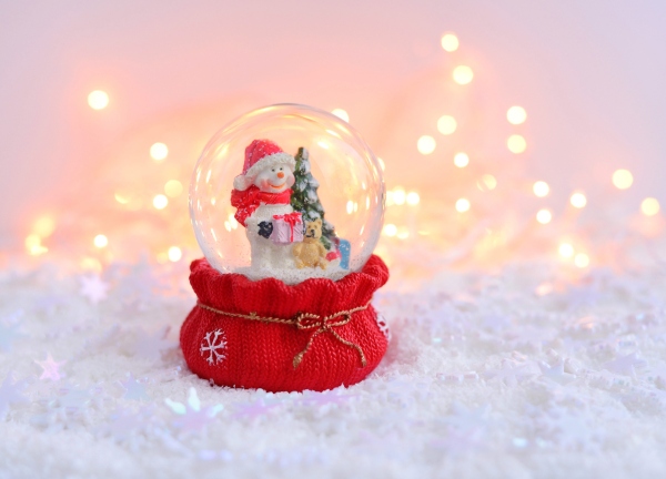 A snow globe with a snowman inside holing a Christmas tree