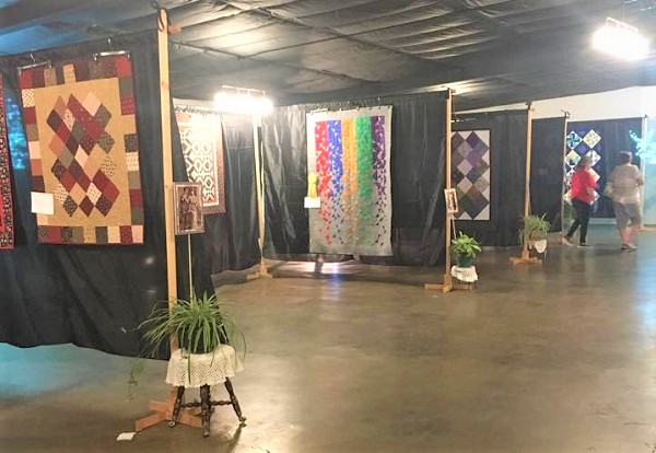 Women walking through hanging quilts at a show.